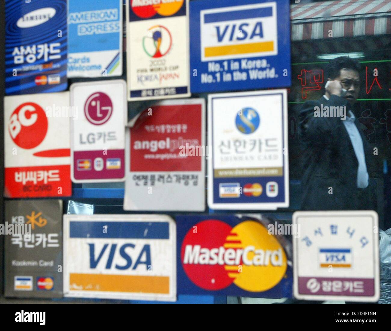 An image of a pedestrian is reflected on a window bearing stickers of  various kinds of credit cards at a restaurant in Seoul May 21, 2003. South  Korea's $97 billion credit card