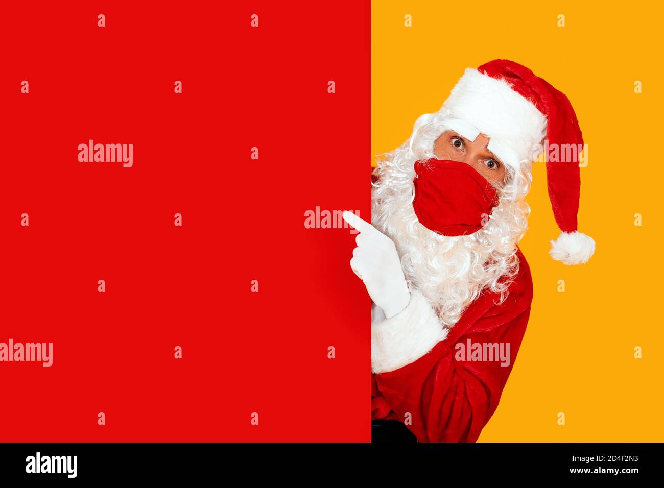 astonished santa claus wearing a red face mask pointing to a red blank space Stock Photo