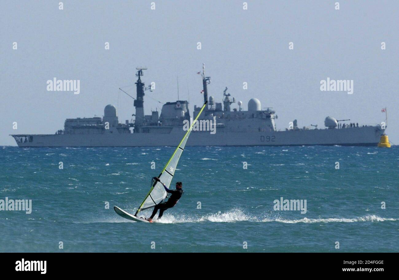 A windsurfer practices in front of a British frigate docked off a coast of northern town of Limassol at the island of Cyprus January 27, 2003. A British fleet, the largest since the Falklands' War in 1982, led by the navy's flagship, aircraft carrier HMS Ark Royal, arrived in the east Mediterranean for exercises on Monday. REUTERS/Yiorgos Karahalis  YK/AA Stock Photo