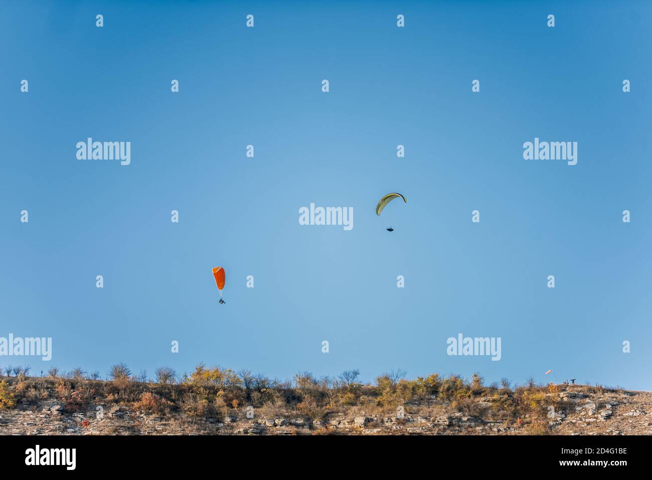 Paragliders with multi-colored parachutes fly high in the clear blue sky over steep cliffs. Parachuting, adrenalitis, love of height, risk, freedom Stock Photo