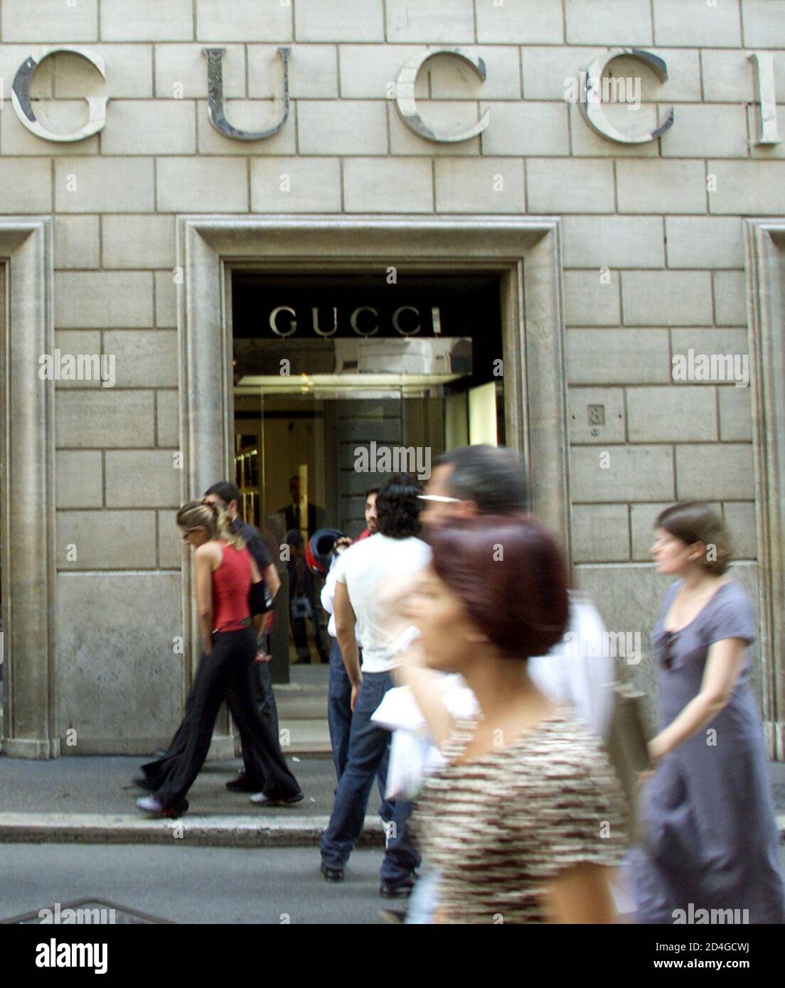 People stroll past a Gucci shop in central Rome June 19, 2001. Italian  luxury goods maker Gucci Group NV warned on Tuesday that both sales and  operating profit would fall short of