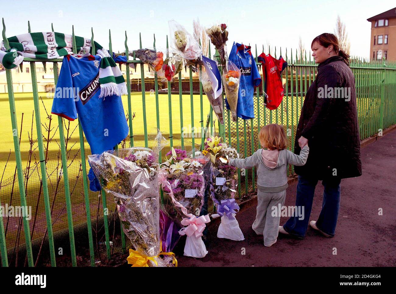 A woman and child look at flowers and Rangers' football shirts hanging from a fence in Kenmure Street, Glasgow, where 15-year-old murder victim Kriss Donald was snatched by a group of men near his home, March 17, 2004. Donald was snatched on Monday by five men said by police to be of Asian appearance, in southern Glasgow and his badly beaten body was found the next day behind a Celtic supporters' club in the east end of the city. REUTERS/Jeff J Mitchell  JJM/MD/THI Stock Photo