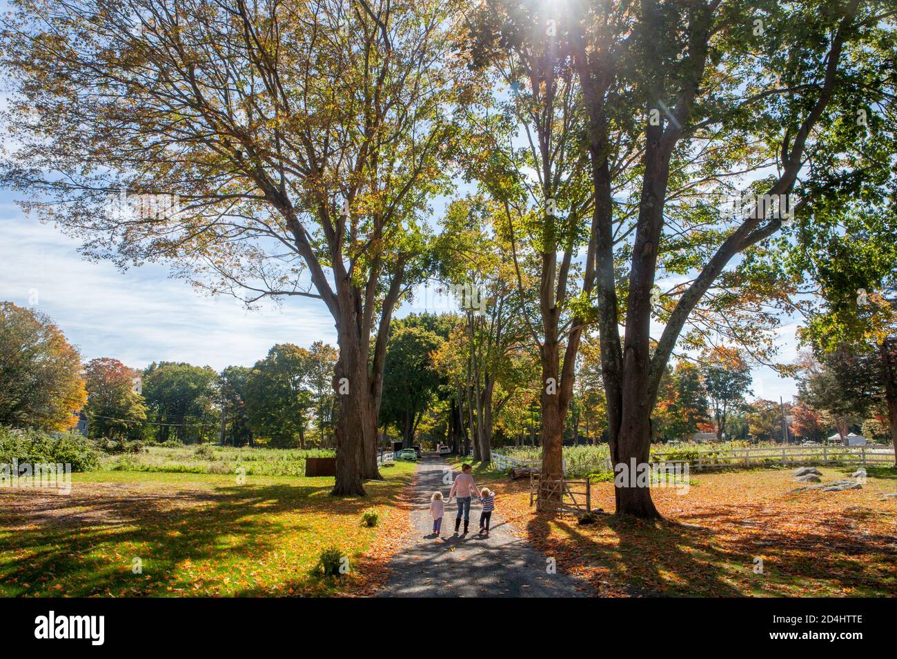A mother and her two young kids walk hand-in-hand down the long gravel driveway of a farm on a sunny fall day in Madison, CT, USA Stock Photo