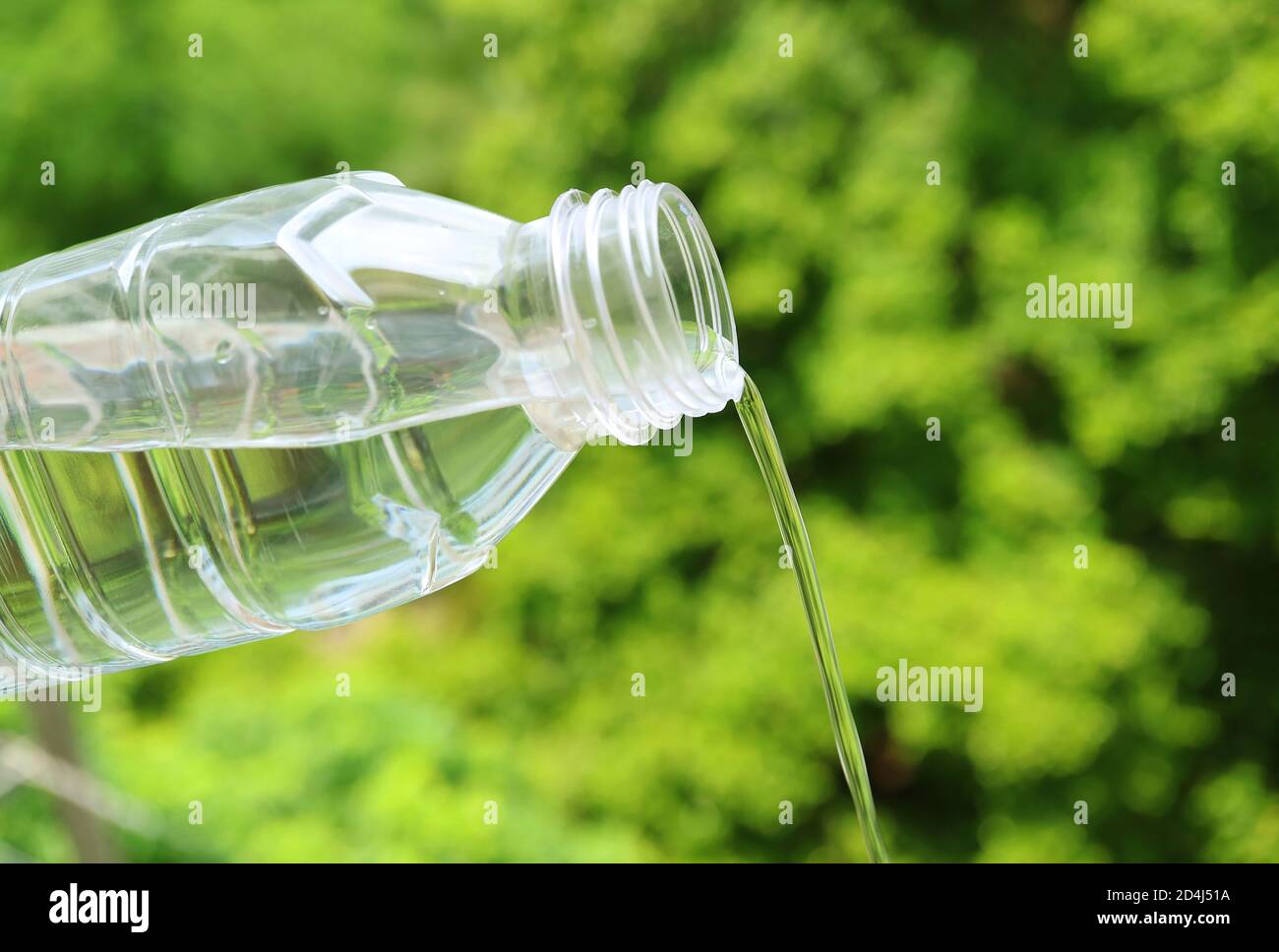 Drinking water pouring from a plastic bottle with blurry green foliage in the backdrop Stock Photo