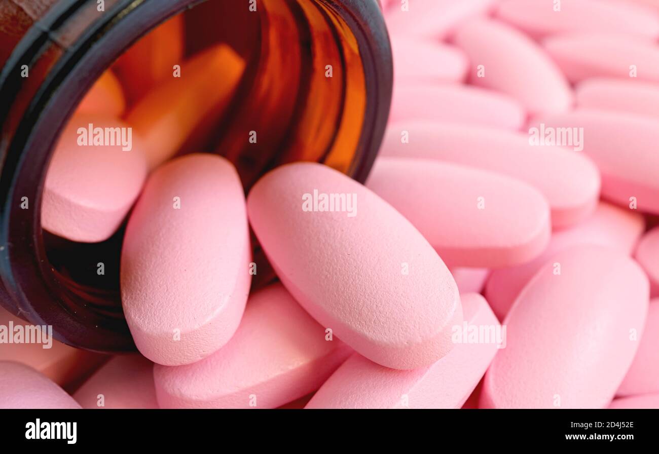 Closeup pink oval shaped pills scattered from the glass bottle Stock Photo