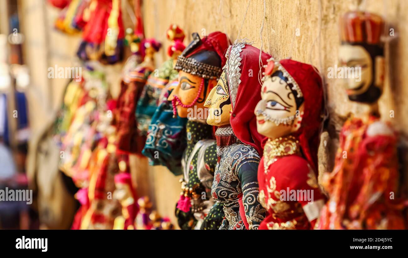 Colorful human face shaped Puppets wearing colorful clothes hanging against the wall in Rajasthan India on 21 February 2018 Stock Photo