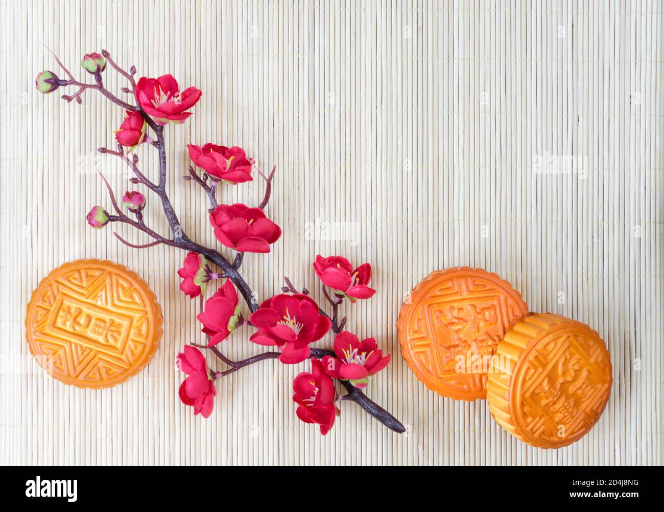 Chinese Mid-Autumn festival composition: traditional chinese moon cakes and branch with red flowers are on a straw mat, with copy-space Stock Photo