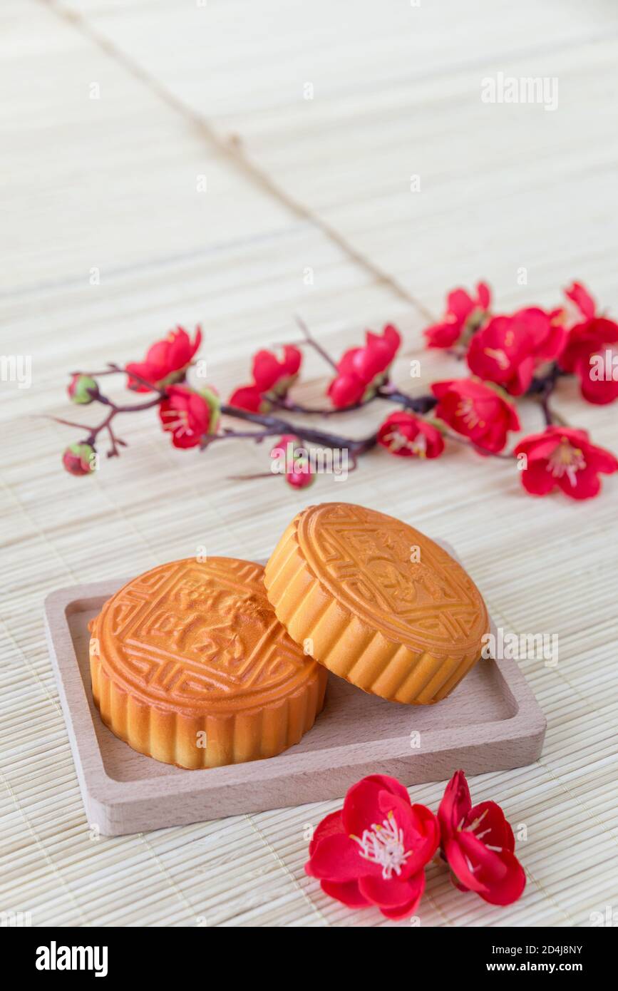 Chinese Mid-Autumn festival composition: traditional chinese moon cakes and branch with red flowers are on a straw mat, with copy-space Stock Photo