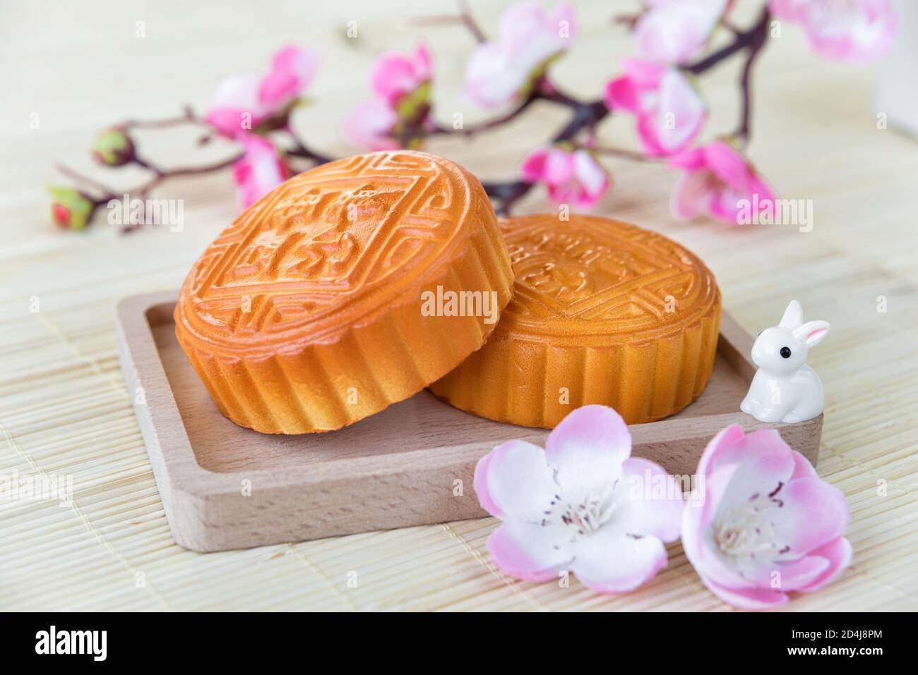 Chinese Mid-Autumn festival composition: traditional chinese moon cakes, moon hare and branch with pink flowers are on a light straw mat Stock Photo