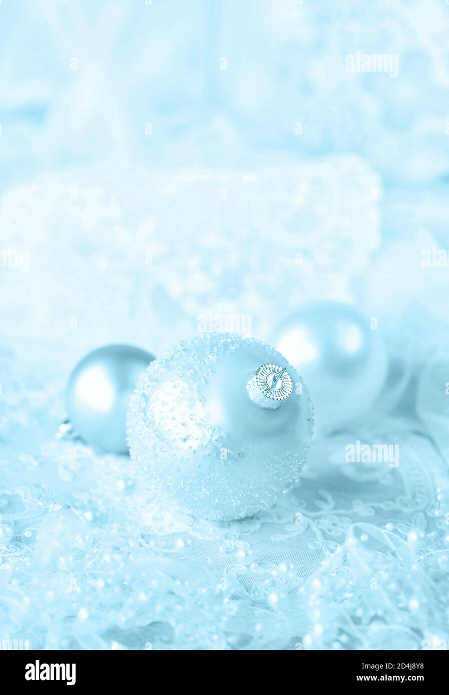 Beautiful Christmas decoration in white and blue colors: several Christmas balls with white ribbon and pearls on a light lacy background; vertical ima Stock Photo