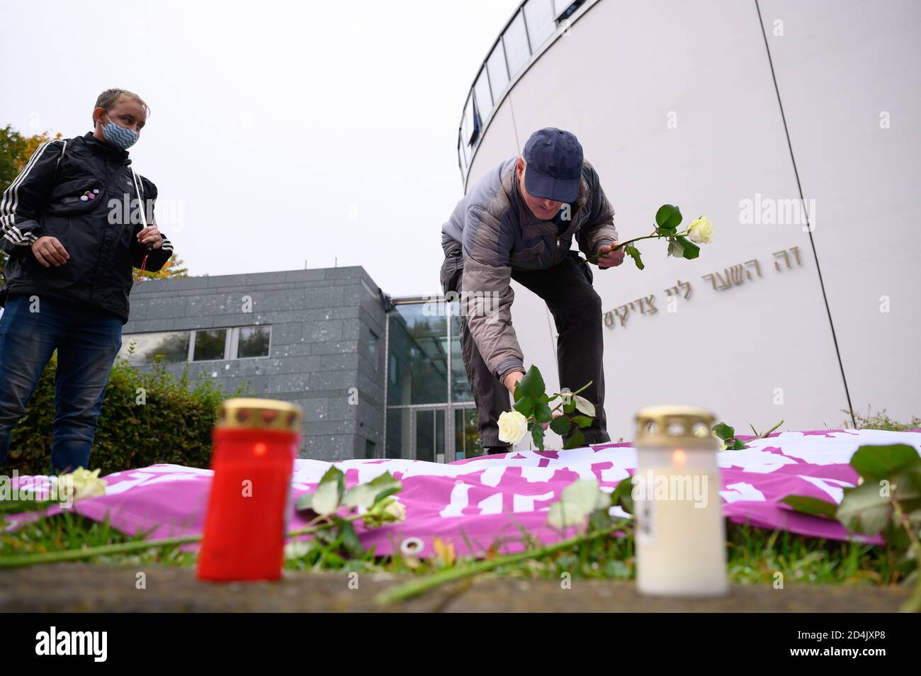 Chemnitz, Germany. 09th Oct, 2020. A participant in a vigil places white roses on a banner in front of the synagogue to commemorate the victims of the right-wing terrorist attack in Halle. On 9 October 2019 a heavily armed right-wing extremist had tried to storm the synagogue and cause a massacre among 52 visitors. When he failed to do so, he shot a passer-by and in a kebab bite a young man. Credit: Sebastian Kahnert/dpa-Zentralbild/dpa/Alamy Live News Stock Photo