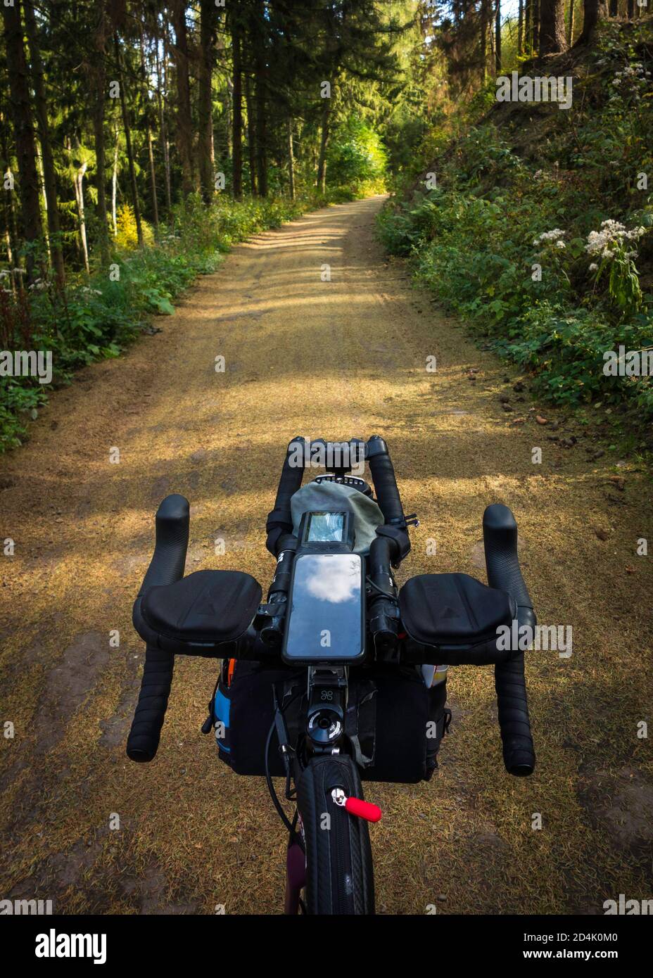 Looking from riders point of view over a bicycle handlebar with drop bars and aerobars and smart devices (phone + bike computer) onto a forest road. Stock Photo