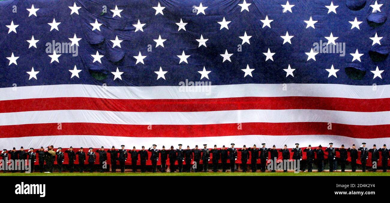Members of all the United States armed services stand underneath a giant United States flag draped across Fenway Park's famed "Green Monster" left field wall as the U.S. national anthem is played before the Red Sox scheduled home opener game April 11, 2003 in Boston. The baseball game between the Boston Red Sox and the Baltimore Orioles was called off and delayed until another day due to heavy rain. REUTERS/Jim Bourg JRB Stock Photo
