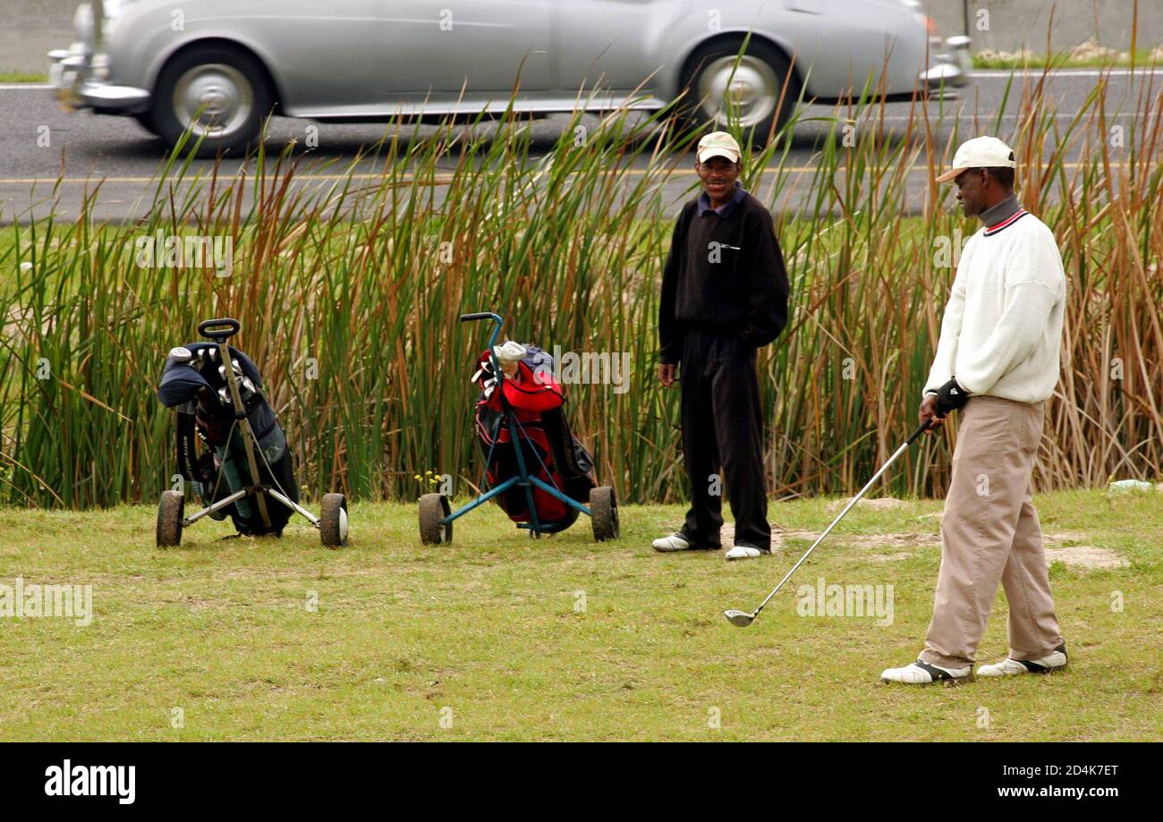 Golf enthusiasts David Ventfolo (L) and Simon Toto (R) play on a makeshift  golf course wedged between Cape Town's busiest motorway and township  shacks, August 3, 2004. A small group of black