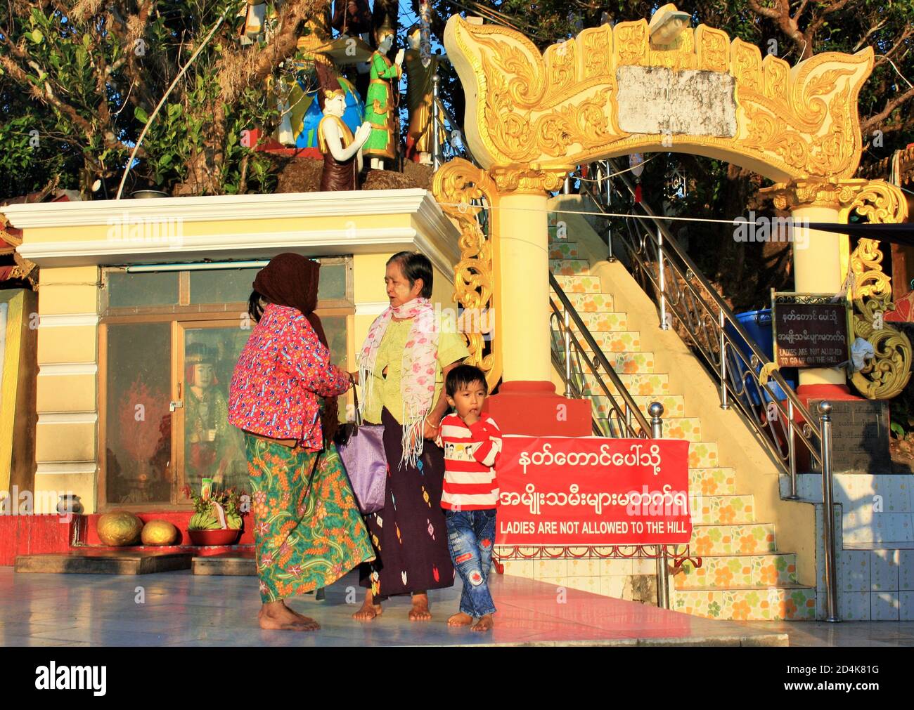 Kyaikto, Mon State Myanmar - December 5, 2019: Two Burmese women and a child standing next to a sign that says 'Ladies are not allowed to the hill' Stock Photo