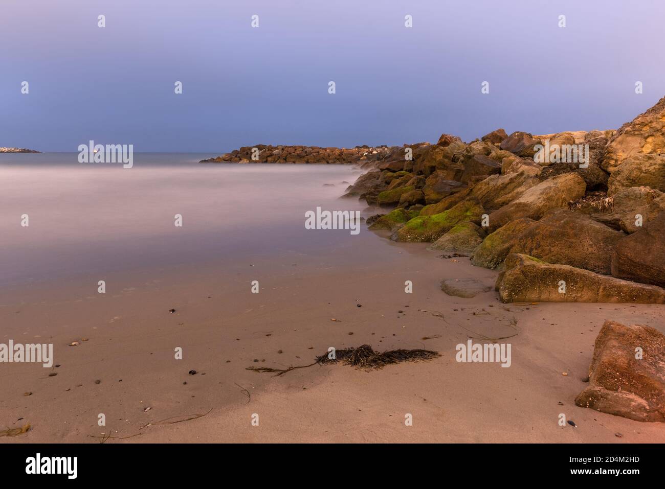 Low tide leaves wet sand near rock boulder jetty as ocean water ...