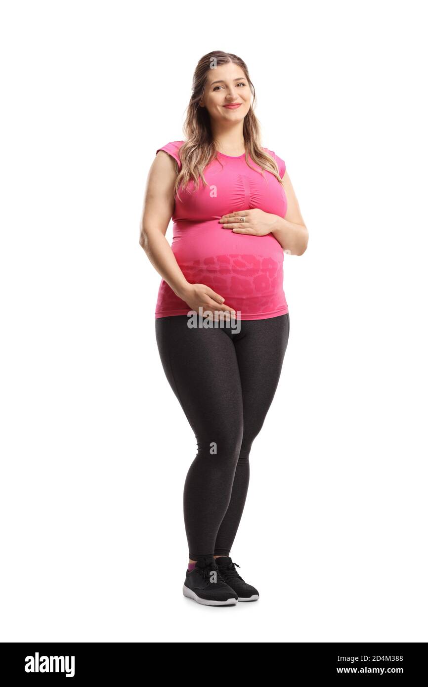 Full length portrait of a pregnant woman in pink top and leggings smiling and holding her belly isolated on white background Stock Photo