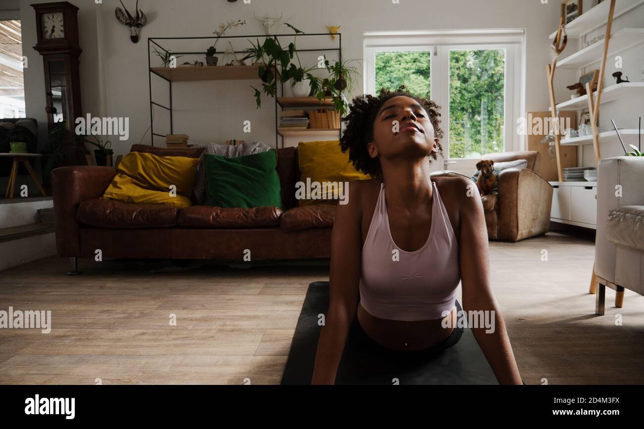 Beautiful young woman working out from home, upward dog stretch, yoga in the lounge Stock Photo