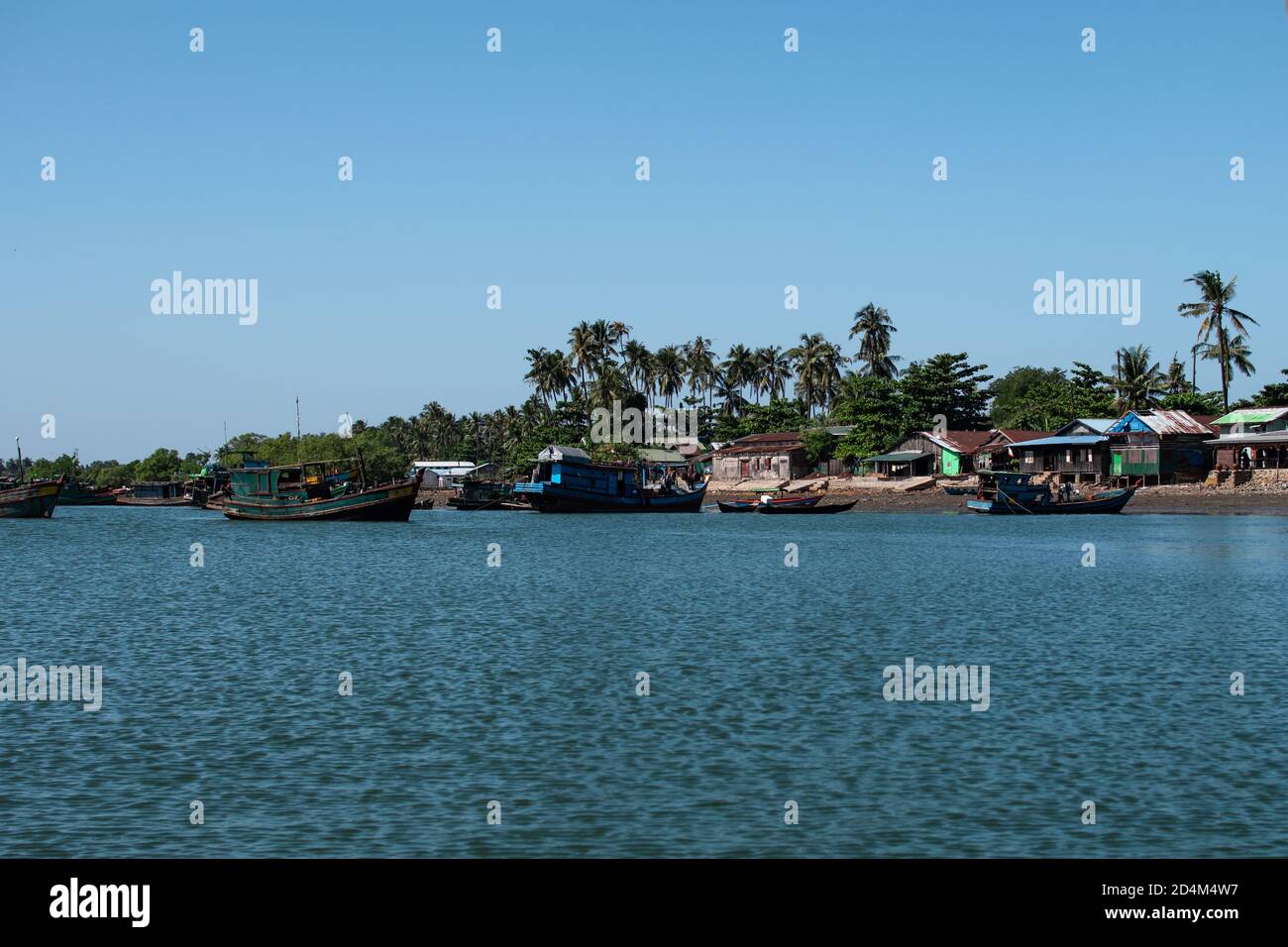 Several traditional wooden boats in a river and houses on the shore by the fishing village Chaung Thar, Irrawaddy, western Myanmar Stock Photo