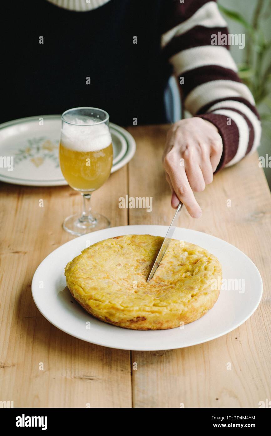 Hand cutting a Spanish tortilla with a beer glass on a wooden table Stock Photo