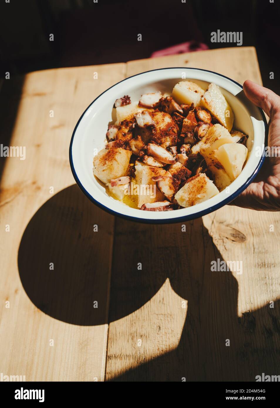 Plate of octopus with potatoes or 'pulpo a la Gallega' in the sunshine casting shadow on a wooden table Stock Photo
