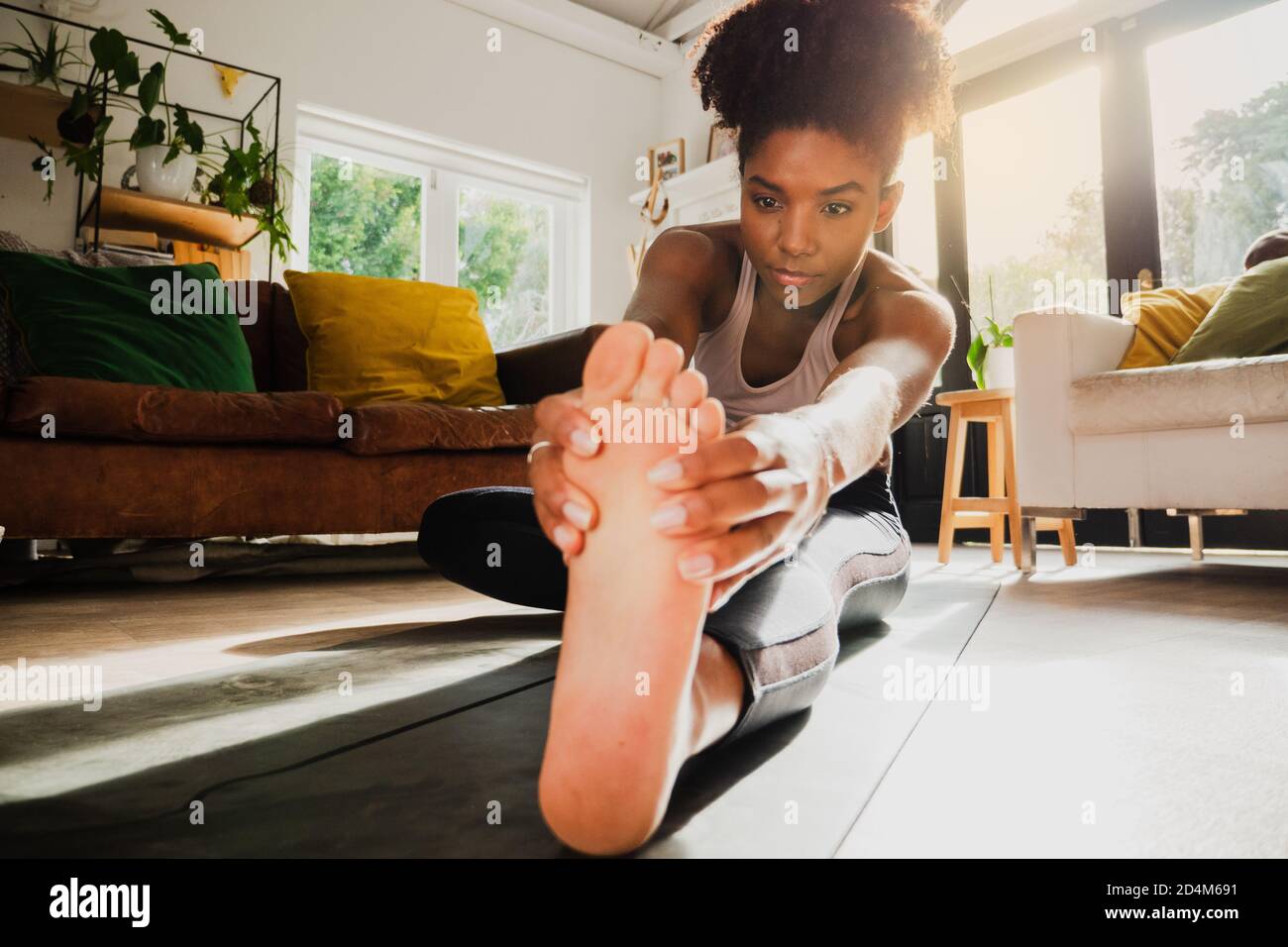 Young female working out from home and stretching legs on yoga mat ...