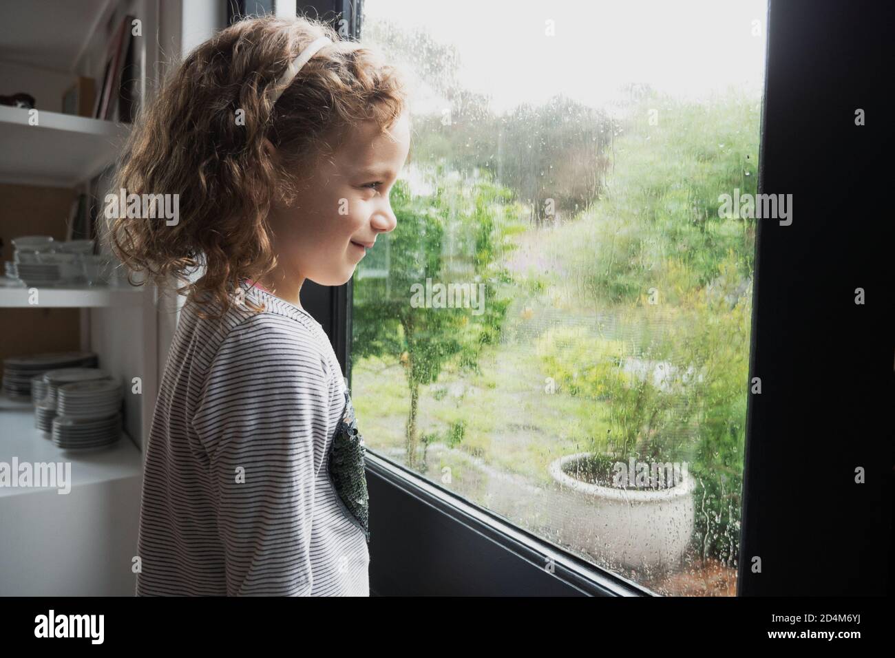 Little caucasian girl looking out at the rain on a stormy winter morning Stock Photo