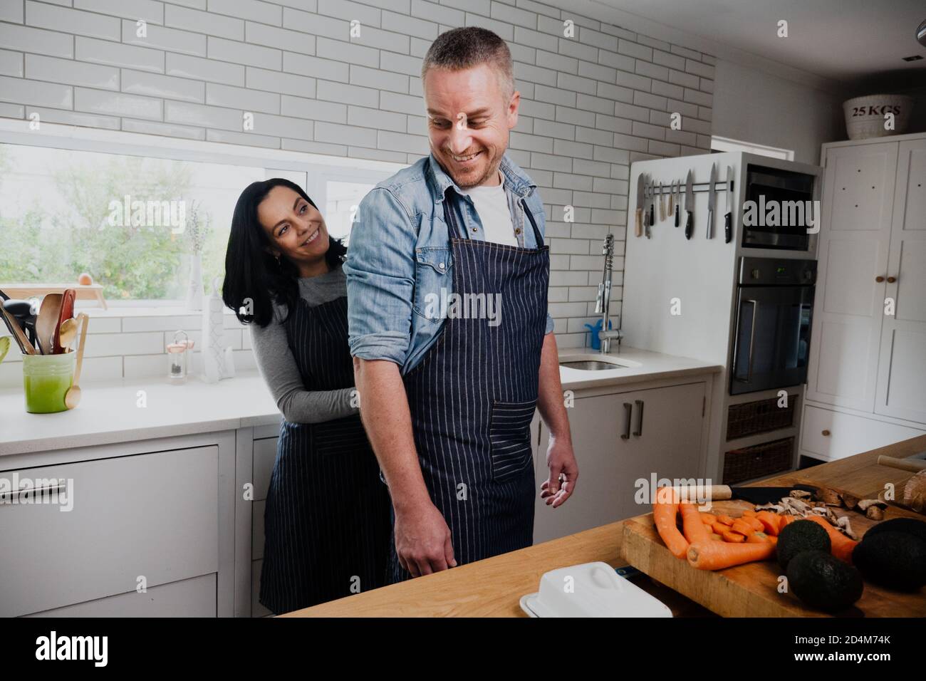 Young couple cooking together, wife helping husband tie his apron in