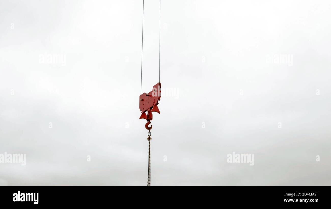 Crane red lifting hook against a white cloudy sky. industrial background concept. Stock Photo