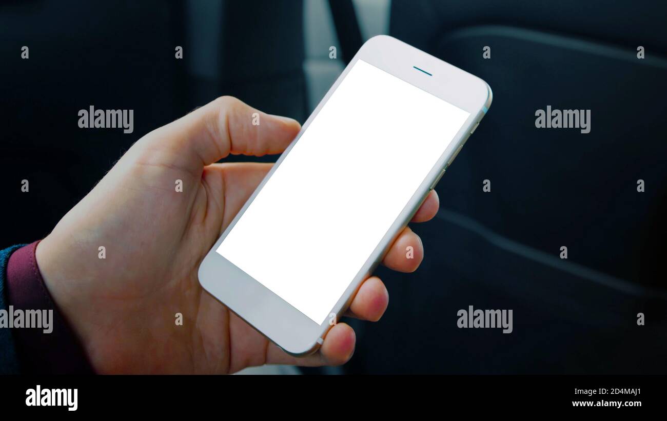Man hand holding a cell phone with a blank white screen smartphone, interior car background, black copy space. Stock Photo