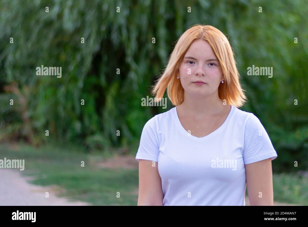 A young woman of blonde Caucasian appearance with brown eyes walks through the park in summer. Close-up, selective focus. Stock Photo