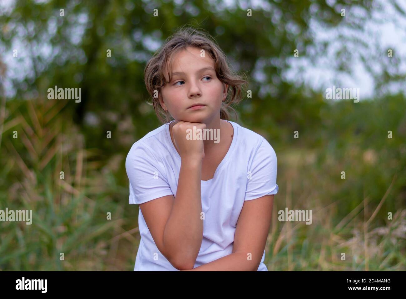 Pensive sad teenager girl looks to the side. Portrait in the park outdoors. Emotions, feelings concept. Blurred background. Stock Photo