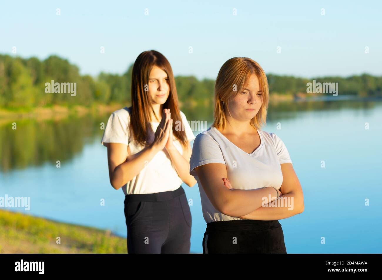 Quarrel of two close friends on a walk near the river, misunderstanding. A young woman is offended and does not want a dialogue, the other begs Stock Photo