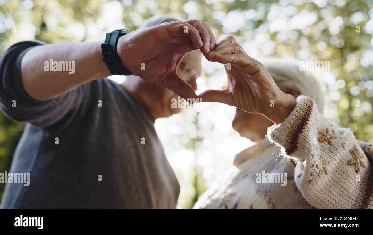 Lovely older retired couple making heart with their hands and looking at each other. Selective focus. High quality photo Stock Photo