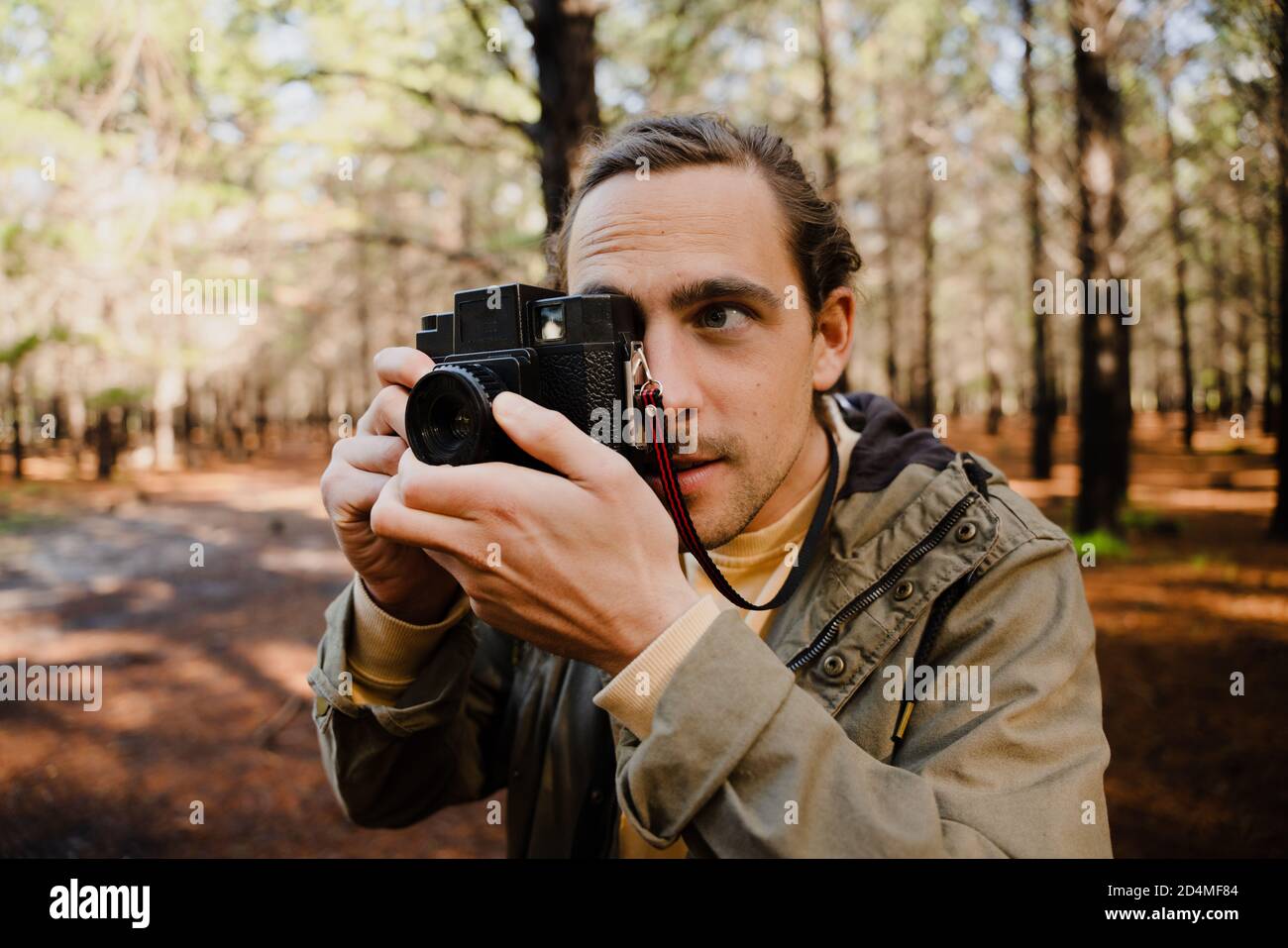 Young male photographer focussing while taking pictures with film camera in bright forest. Stock Photo