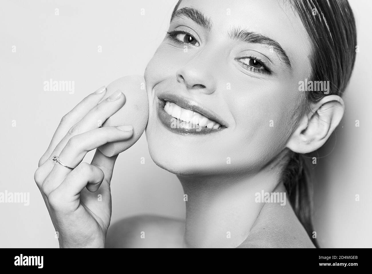 Healthy smiling girl with bare shoulders, clear skin, dark hair and beige sponge. Natural makeup look. Health and beauty concept. Happy young woman Stock Photo