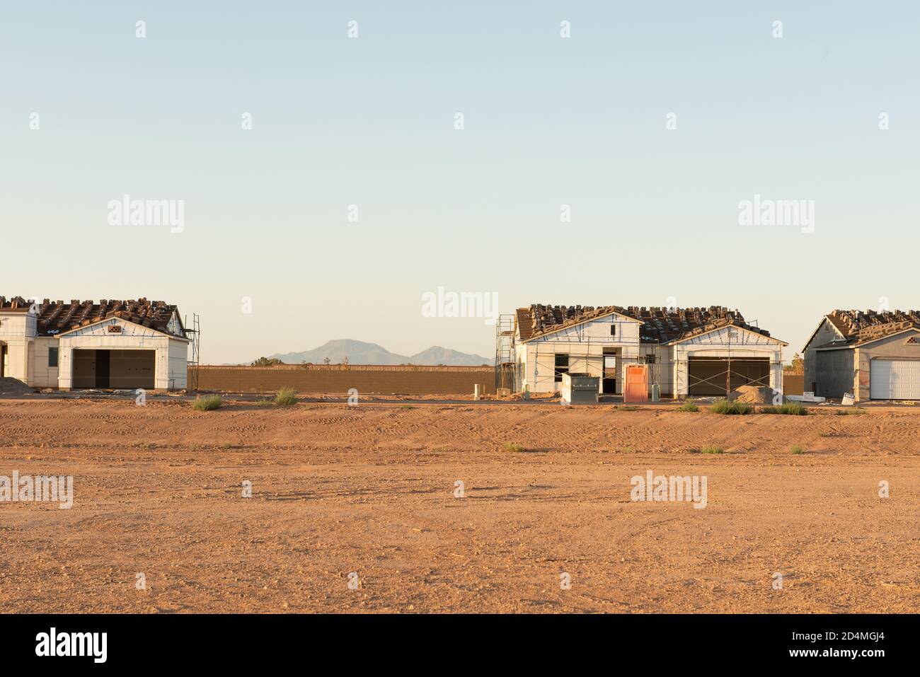 A row of houses being constructed on a dirt lot with an empty lot between and view of the mountains in background stands in central Arizona building boom. Stock Photo