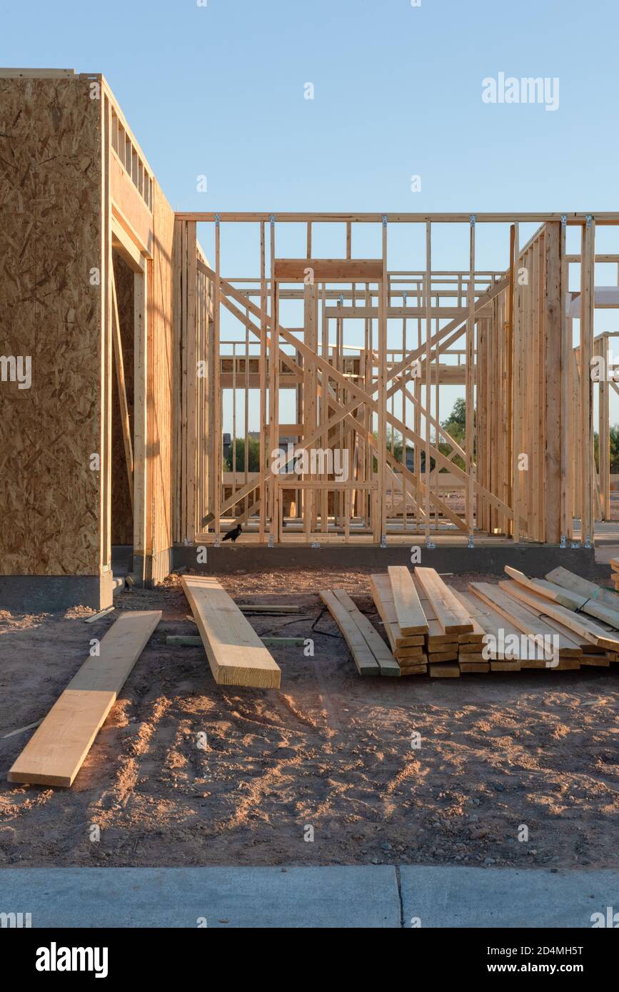A partial view of a new house construction showing the wood frame before the siding and roofing stands in early morning light on a dirt lot, vertical view. Stock Photo
