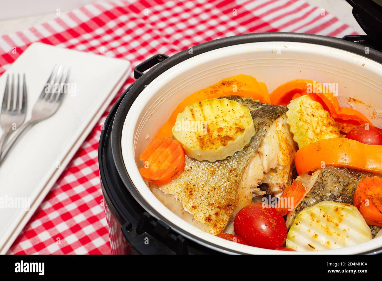 Fish  with vegetables steam cooking. pieces of boiled fish and vegetables in a double boiler. Red checkered tablecloth Stock Photo