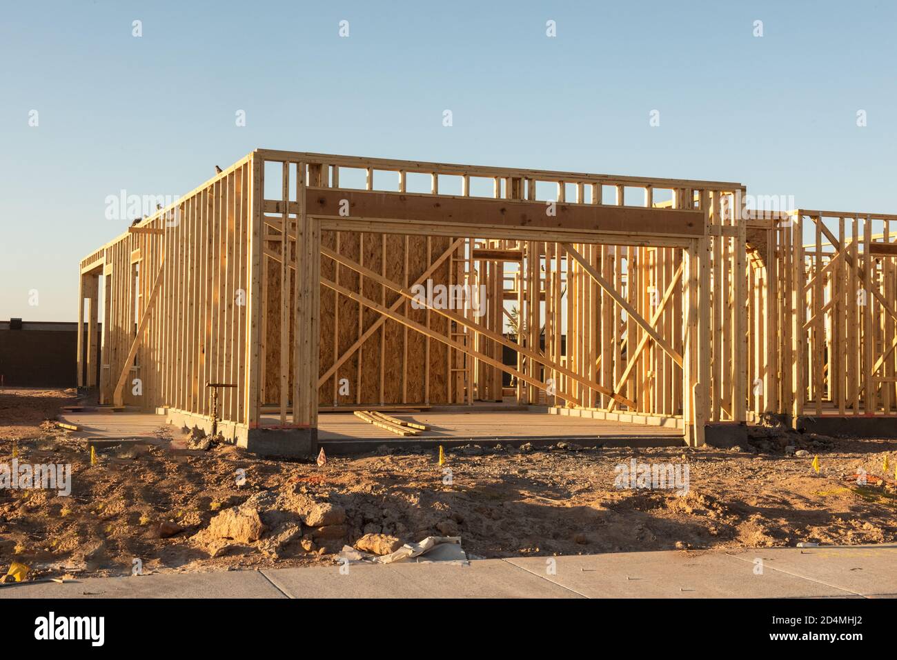 A partial view of a new house construction showing the wood frame before the siding and roofing stands in early morning light on a dirt lot, horizontal view. Stock Photo