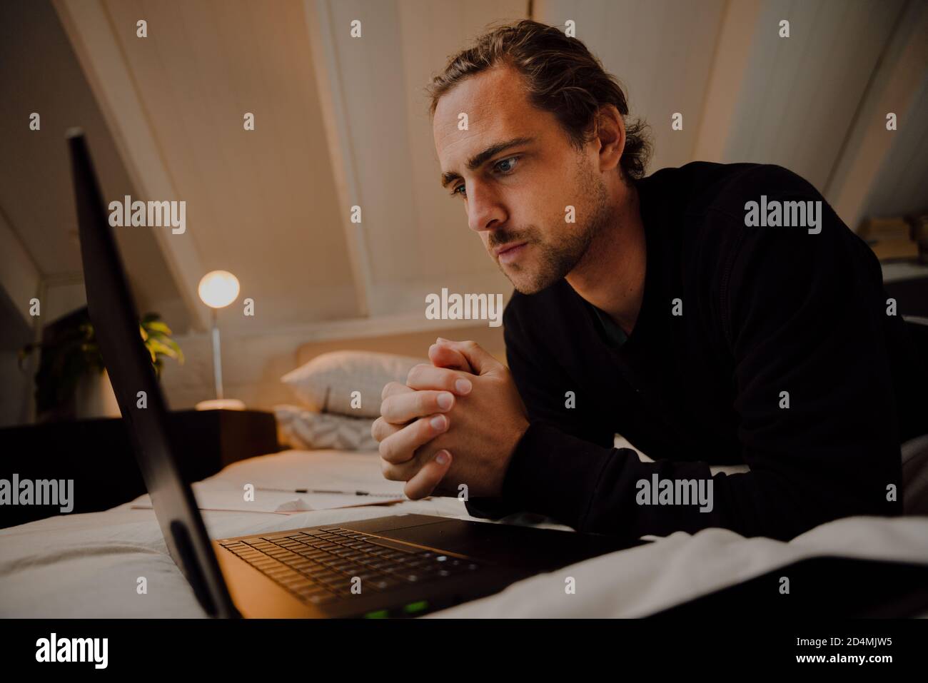 Young caucasian male student hoping he passes exams while looking at results on the computer at home on the bed Stock Photo