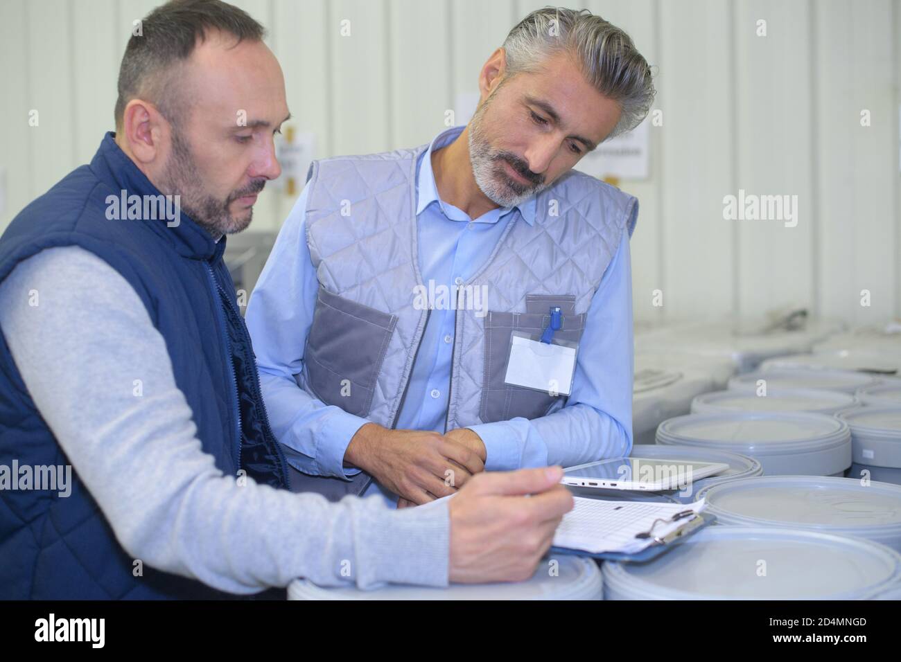 manager noting on clipboard and worker taping box in warehouse Stock Photo