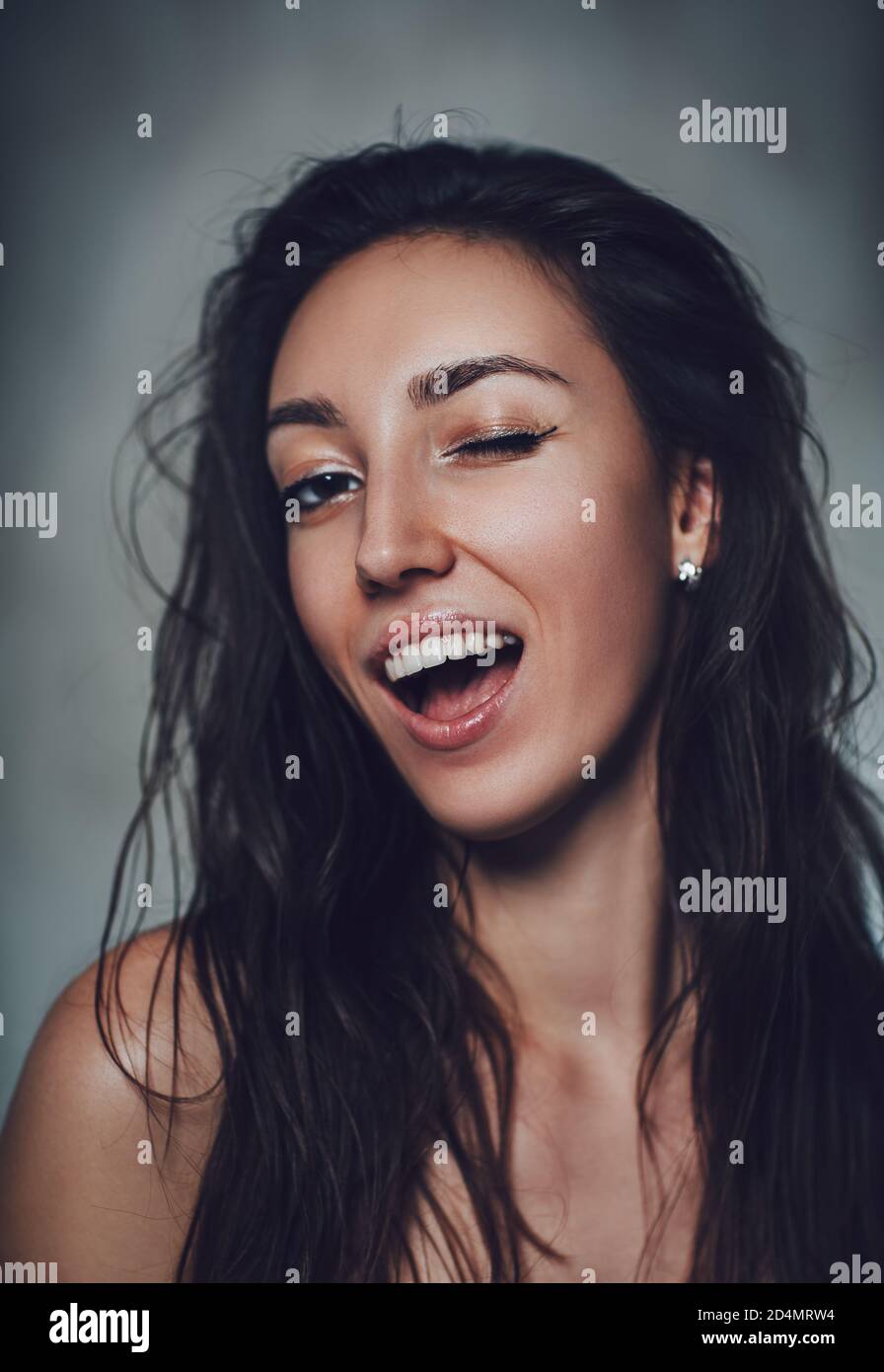 Young Brunette Woman Winking Emotional Portrait On Gray Wall Background