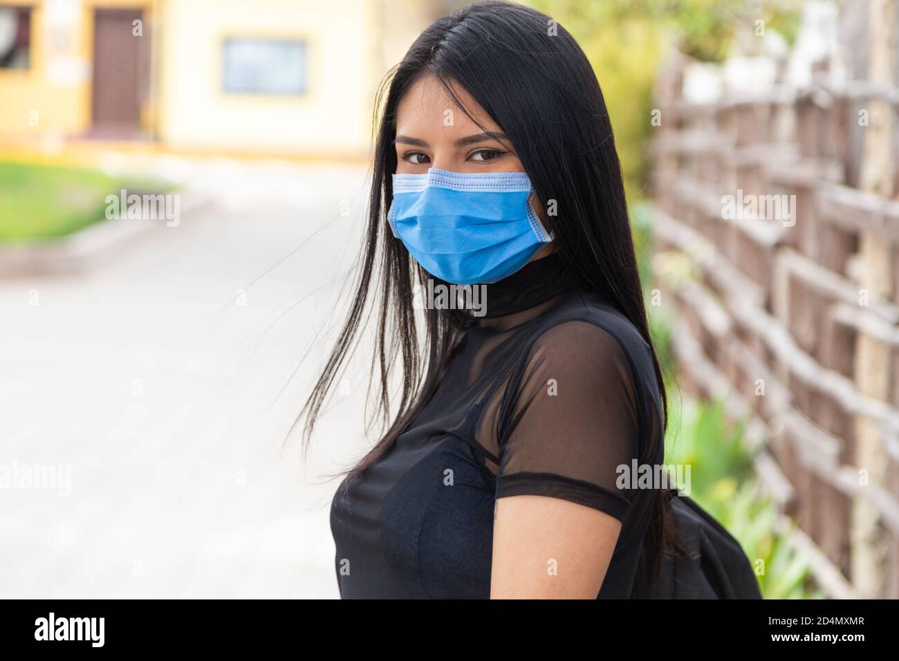 closeup to face of beautiful young latin woman with long black hair, wearing a mask, transparent blouse, outdoors Stock Photo