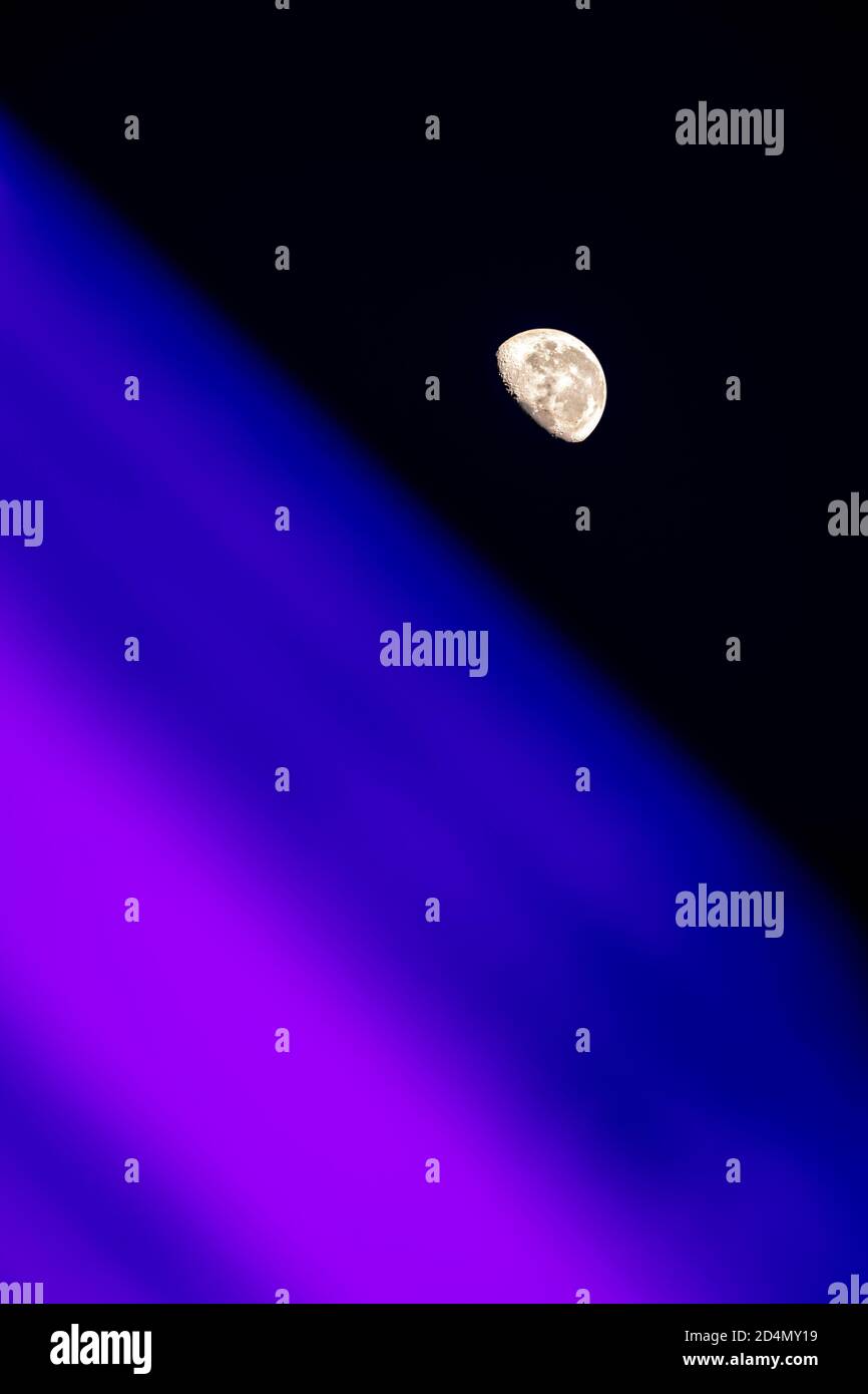 Gibbous moon against clear black skies, with colorful blue and purple blurred planetlike horizon in forgeround Stock Photo