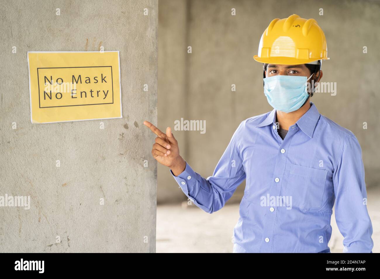 worker pointing No Mask No Entry signage notice board on wall at working construction site to protect from coronavirus or covid-19 at workplaces - Stock Photo