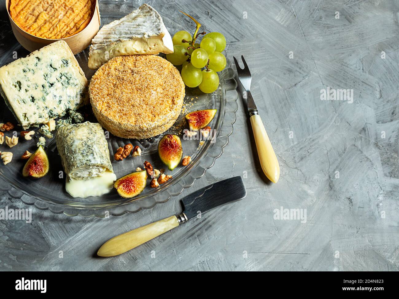 Assortment of French cheese - camembert, roquefort, brie, goat cheese and epoisse with grapes, figs and nuts on a gray background. Top view with copy Stock Photo