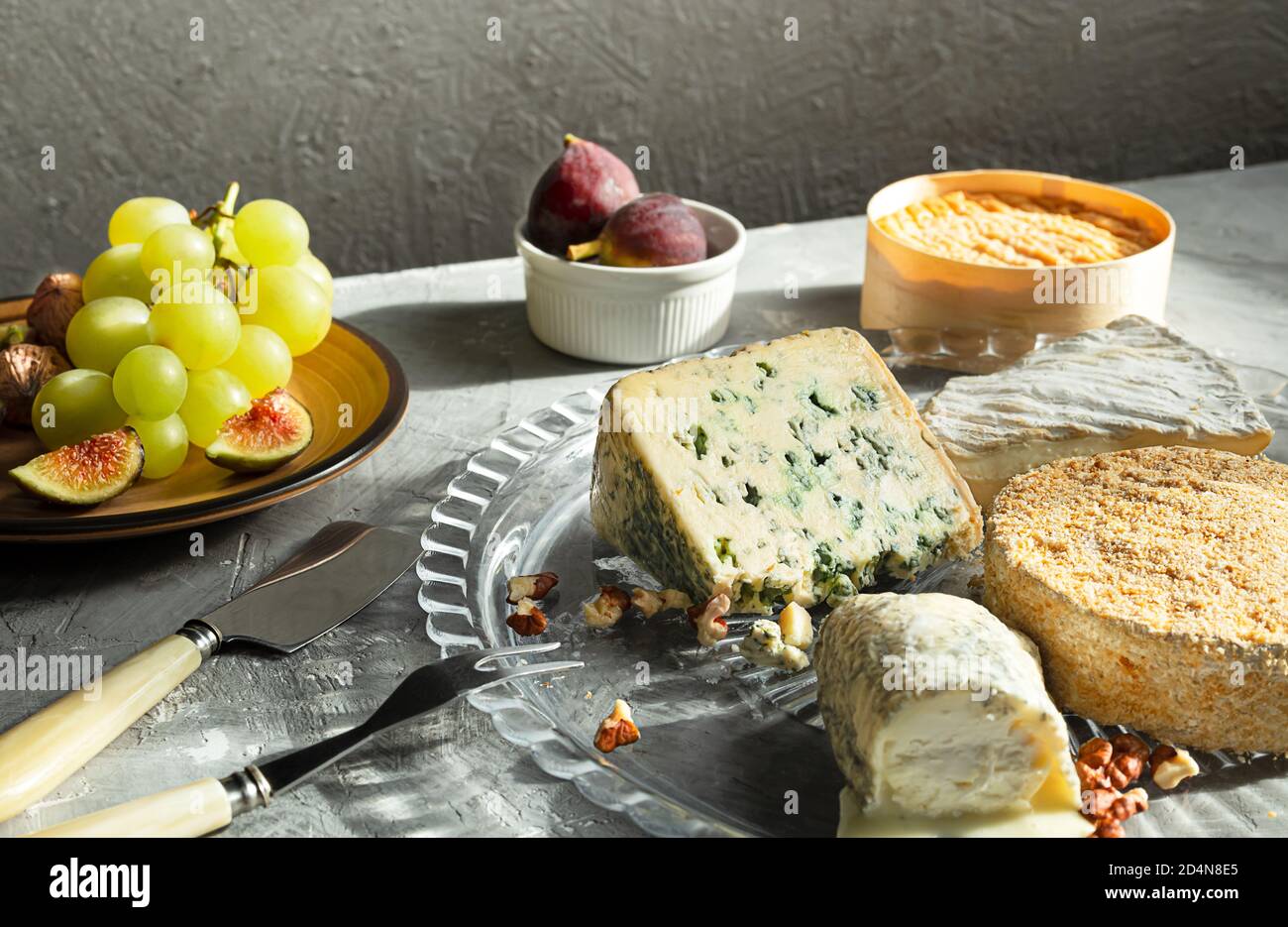 Various types of French cheeses - camembert, roquefort, brie, goat cheese and epoisse with grapes, figs and nuts on a gray background Stock Photo