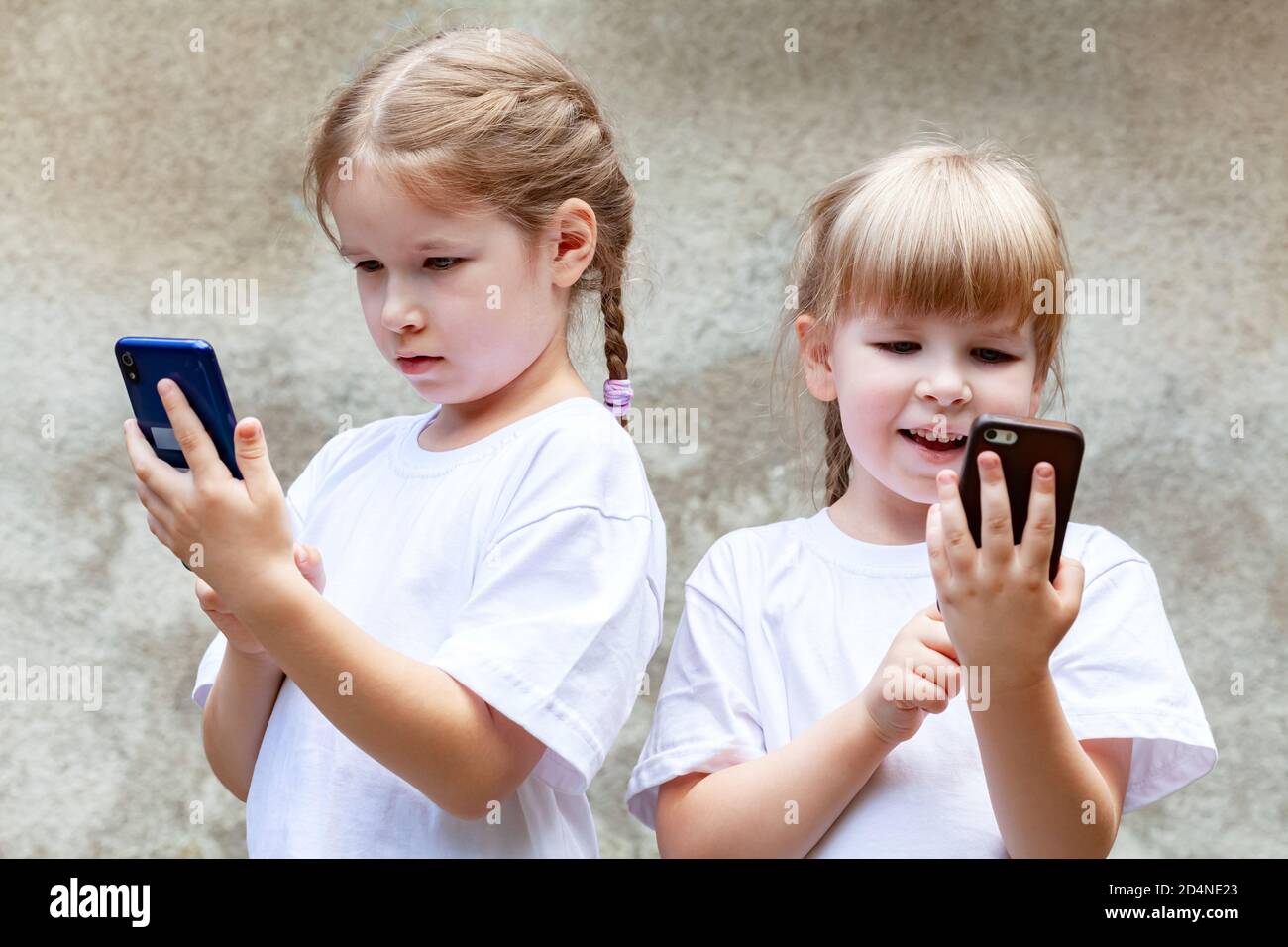 Sisters, young children using modern smartphones, two girls together holding and using their mobile phones, playing around. Tech savvy generation Stock Photo