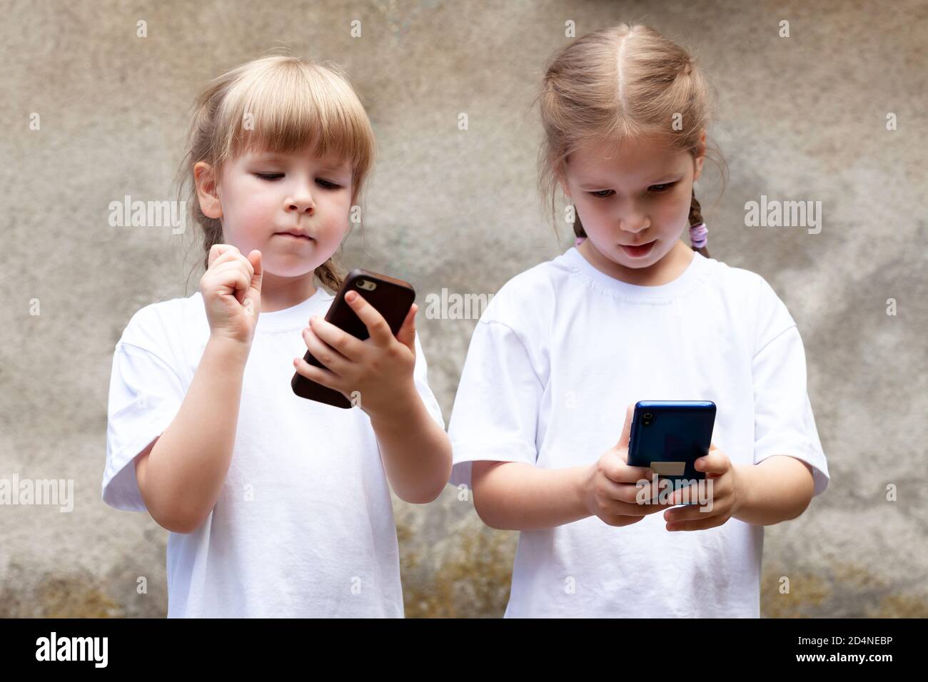 Two little girls, sisters using modern smartphones, young children holding their mobile phones, playing around. New generation, kids and technology Stock Photo